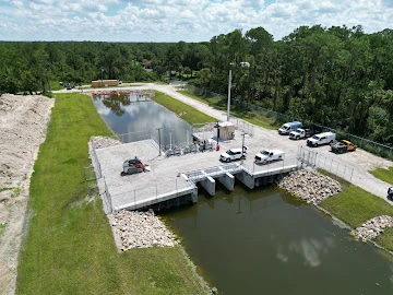 Aerial view of a water-control structure and construction vehicles alongside a canal