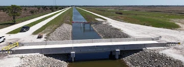 A completed concrete bridge crossing a canal in a broad landscape